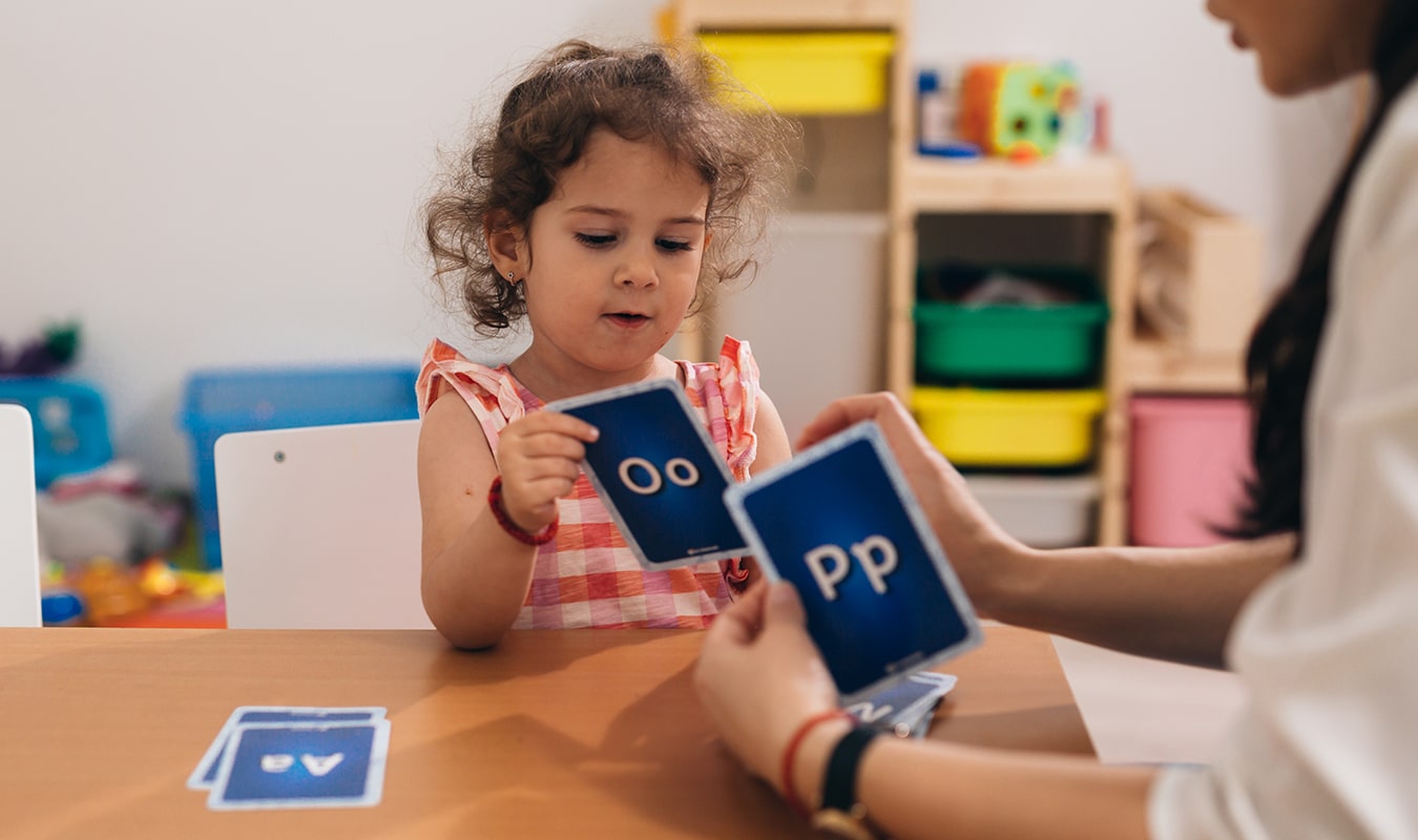 A toddler playing an alphabet card game with a teacher.